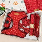 A red and white polka dot dog accessory set displayed inside a branded gift box, including a harness, leash, matching fabric pieces, and a small pouch. The box lid has paw prints and floral motifs.