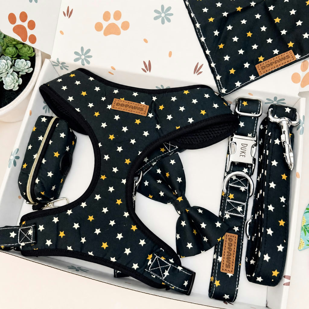 A dog harness set displayed in a gift box, featuring a black harness with a white and yellow star pattern, a matching leash, a small zippered pouch, and a folded blanket. The brand name 'Duke' is visible on the leather patches and hardware.