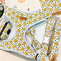 A dog harness set laid out on a light surface, featuring a matching harness, leash, and small pouch. The fabric has a light blue base with a yellow and black spotted pattern, and a small brown leather brand patch reading 'Pup Patterning'.