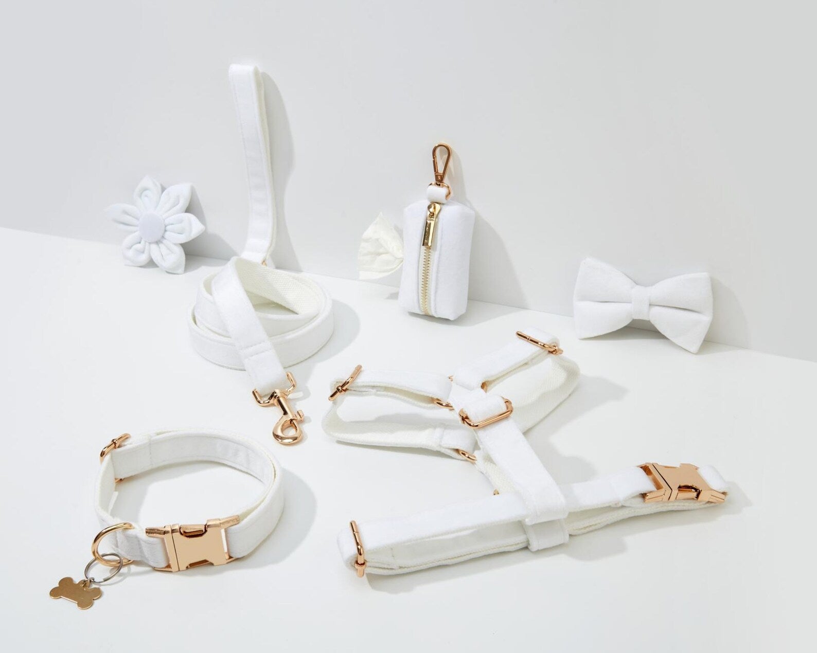 Collection of white pet accessories with gold hardware on a light gray background